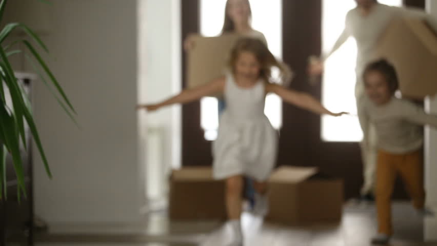 Excited kids boy and girl running into new home with parents holding boxes at background, happy couple with children and packed cardboards just moved in big modern house, family relocating concept Royalty-Free Stock Footage #31060996