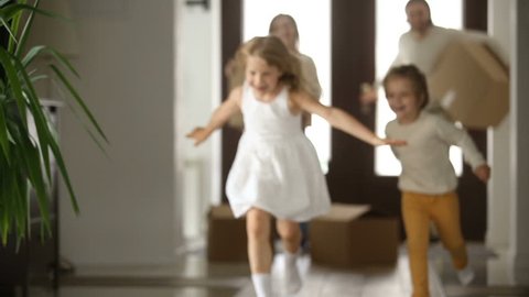 Excited kids boy and girl running into new home with parents holding boxes at background, happy couple with children and packed cardboards just moved in big modern house, family relocating concept