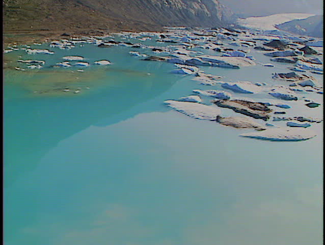 Low level fly over alpine lake filled with melting icebergs from mountain