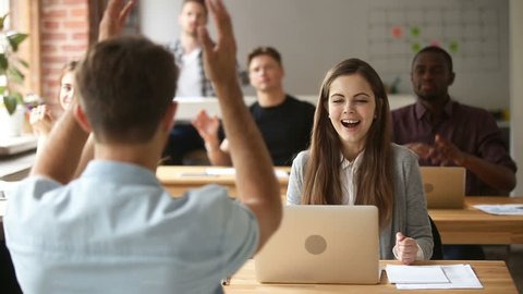 Multi-ethnic team cheering female coworker looking at laptop celebrating success in coworking, applauding colleagues congratulating excited businesswoman with achievement or business win in office