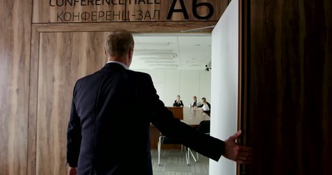 Mature businessman in formalwear entering office meeting room and shaking hands with collegue
