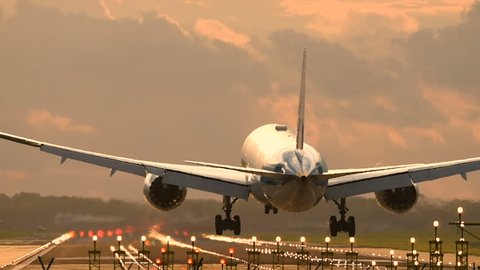 Passenger airplane landing towards the runway during sunset.