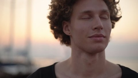 Caucasian curly guy opens eyes smile with affection, evening blue sky. Cloeup, slow motion