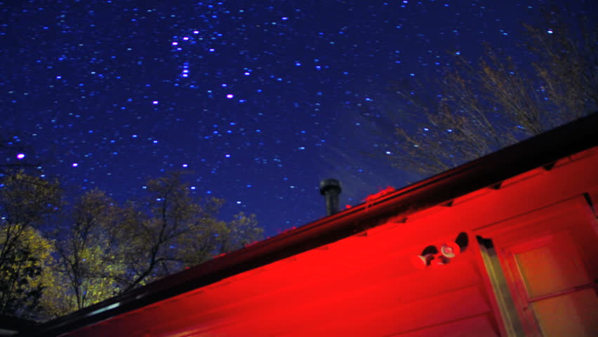 Star Trails Pass Over Red Cabin Cottage in Blue Night Sky Timelapse