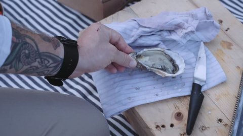 Chef man with tattooed arms prepares beautiful picnic setup, cutting and opening oysters, seasoned with fresh lemon juice and arranged on antique vintage tray served with ice cubes