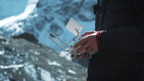 Drone Remote Controlling. Hand and remote view of a drone pilot operator. A traveler in the snowy mountains takes pictures and examines the territory