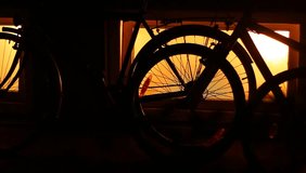 Silhouettes of bicycles parked near window with orange light, leaning against the wall. Night scene. Beautiful shadows and silhouettes of bicycles. Secured. Anti theft. Locked. Safe. Theft proof.