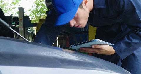 In a garage a mechanic using the tablet makes the oil and engine check to the car smiles. Concept of: security, safety, insurance and professionalism, revisions, technology.