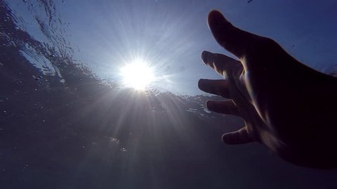 Male hand stretches from under the water to sunrays. Arm asking for help and trying to reach to the sun. Point of view of man drowning in the sea or ocean and floating to the surface. Slow motion POV