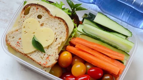 Healthy lunch box with sandwich and fresh vegetables, bottle of water.