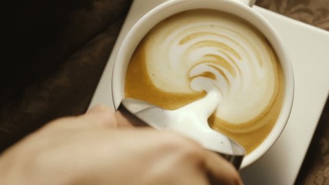 Pours milk into a coffee cup in a cafe