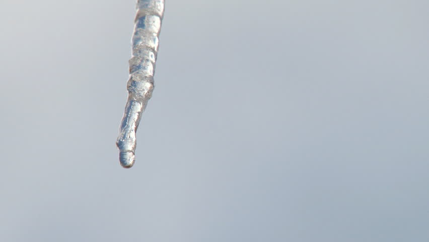 A solitary icicle drips meltwater as blurred clouds pass by overhead.