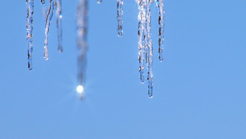 Dripping icicles, rack focus from far to near against blue sky. Additional glint