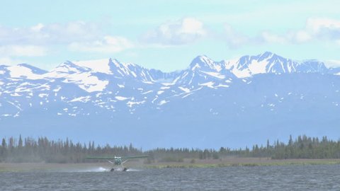 A pretty, green DeHavilland Beaver floatplane takes off from Beluga Lake in Homer, Alaska. The Kenai Mountains loom beyond.