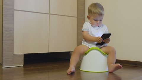 Little boy pisses in his potty and looks at the telephone