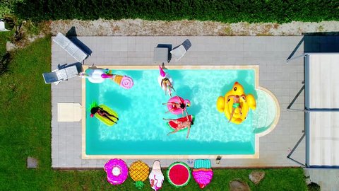 Group of friends having fun on the air mattress in the swimming pool. Different inflatable beds of various colors and shapes