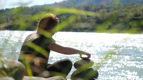 Young woman with red hairs relaxing putting pebble stack next to the mountain river. 3840x2160