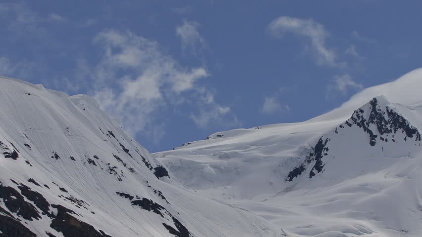 Ridge line over a small glacier, snowy, shrouded by time lapse clouds.