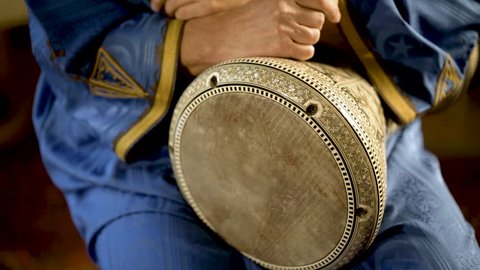 Tight shot of man in Moroccan dress playing arabic doumbek, darbuka