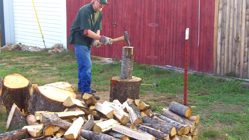 A middle aged or mature man splits logs for firewood.