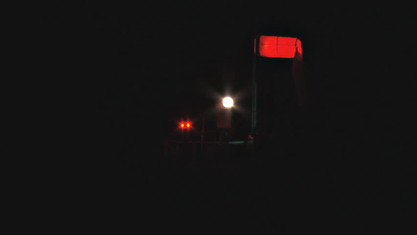 Rotating airport light assembly on tower at airport. Glowing windsock in still