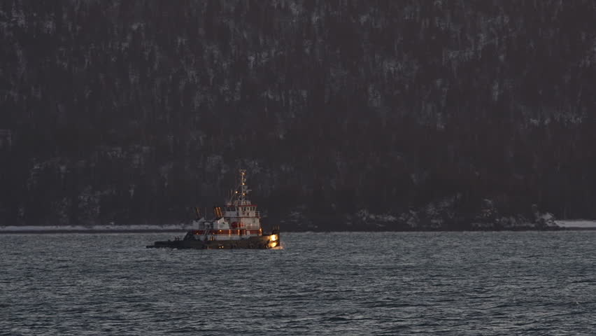 red and white tugboat under way toward the mouth of the bay and the setting sun,