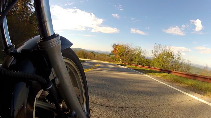A low angle shot of the speeding front tire of a motorcycle on a rural road. 