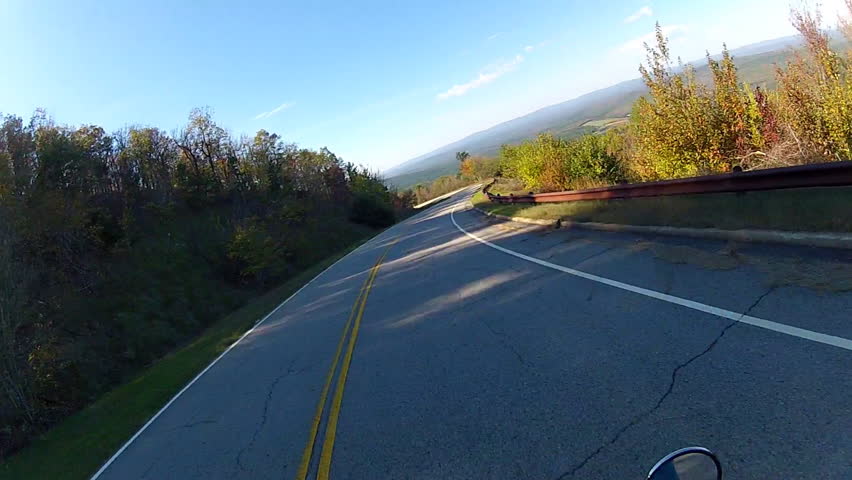A helmet-cam POV shot of a motorcycle speeding down a curvy, forested mountain