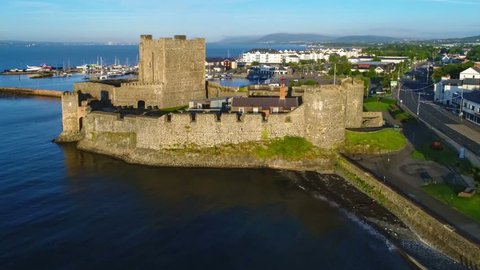 Medieval Norman Castle in Carrickfergus near Belfast, Northern Ireland,  in sunrise light. Aerial flyby video with marina, yachts, parking, town and far view of Belfast in the background