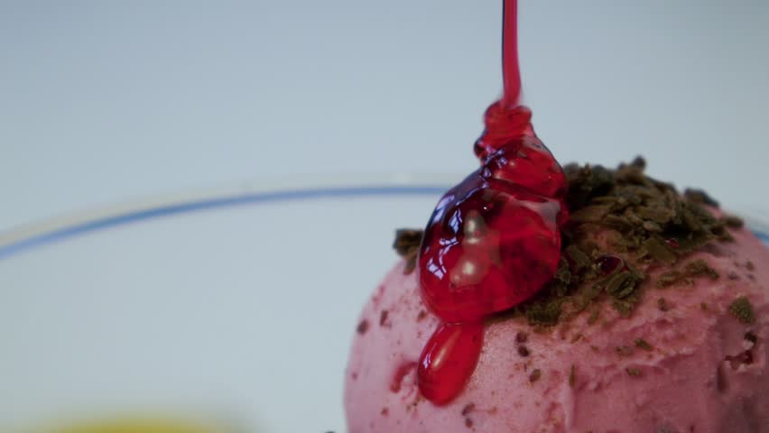 Preparation of Italian ice cream gelato. Balls of colorful ice cream are poured with red jam. Ice cream in a glass. Sweet cold dessert. Strawberry and peach ice cream
