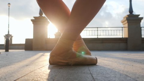 Close up of a ballet dancer's feet as she practices pointe exercises on the stone embankment. Woman's feet in pointe shoes. Ballerina shows classic ballet pas. Slow motion. Flare, gimbal shot