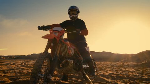 Low Angle Shot of the Professional Motocross Motorcycle Rider Standing on the Path of the Off-Road Track. It's Sunset and Track is Covered with Smoke/ Mist. Shot on RED EPIC-W 8K Helium Cinema Camera.