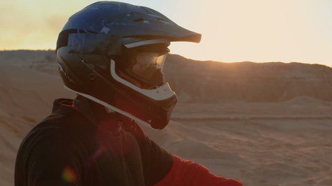 Close-up Portrait Shot Of the Extreme Motocross Rider in a Cool Protective Helmet Standing on the Off-Road Terrain He's About to Overcome. Background is Sandy Track. Shot on RED EPIC-W 8K Camera.