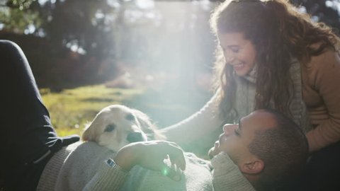 A man and a woman affectionately stroking their pet dog as they relax together outdoors and enjoy the early morning sunshine. In slow motion.