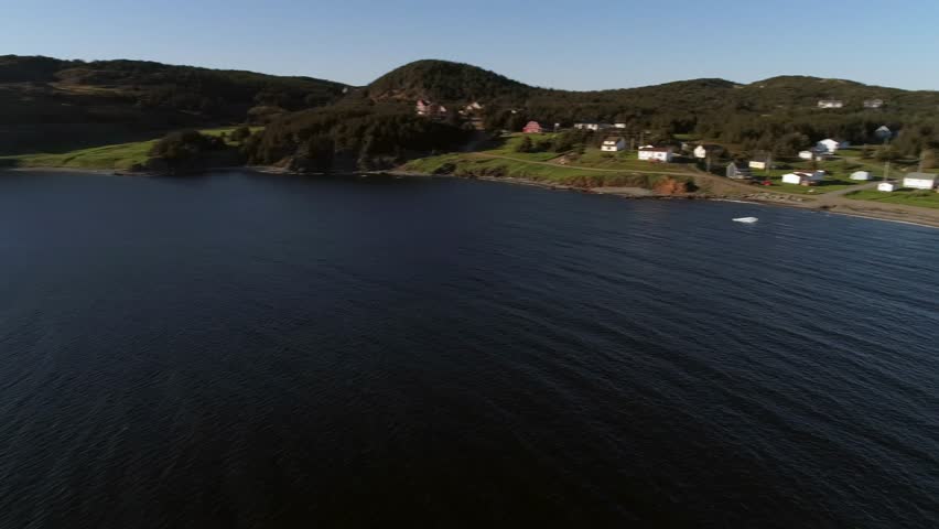 A beautiful aerial shot of ice bergs floating in the ocean water by an island at sunset off the coast of Twillingate Newfoundland Canada