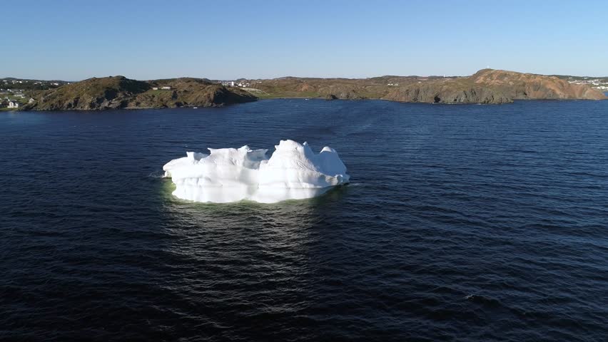 A beautiful aerial shot of ice bergs floating in the ocean water by an island at sunset off the coast of Twillingate Newfoundland Canada