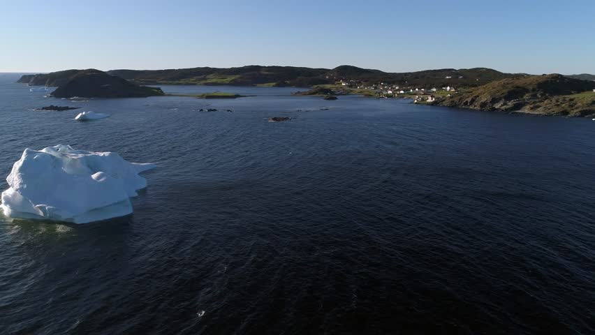 A beautiful aerial shot of ice bergs floating in the ocean water by an island at sunset off the coast of Twillingate Newfoundland Canada