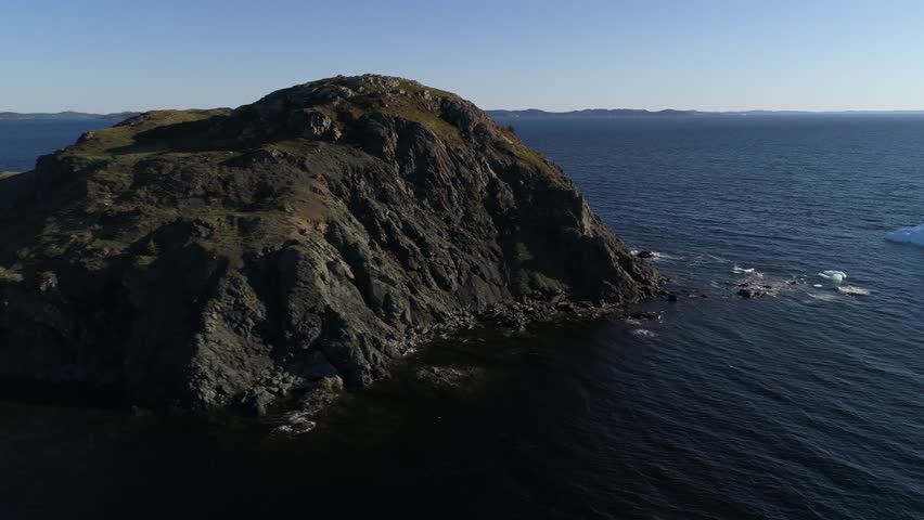 A beautiful aerial shot of ice bergs floating in the ocean water by an island at sunset off the coast of Twillingate Newfoundland Canada