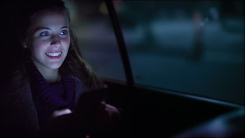 Close up of attractive woman in a car using mobile phone. She is texting, checking mails, chats or the news online. Night.