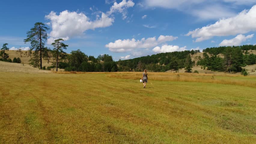 Beautiful young female with white hat enjoying in nature and mountain landscape, golden grass fields, streams and hills at summer