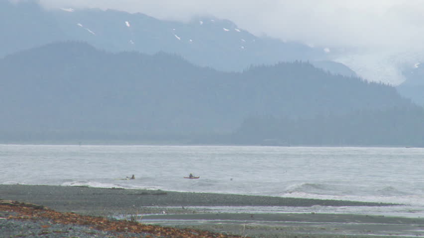 Long shot of kayakers playing in the waves just offshore on a cloudy day.
