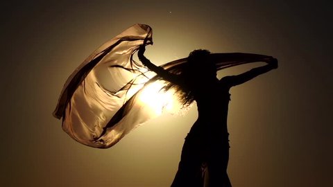 Girl on the seashore gracefully dances her body against the sunset. Silhouette. Slow motion