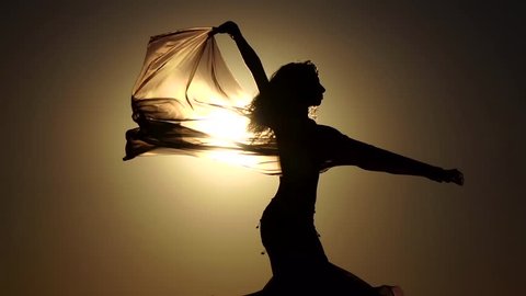 Girl with a veil in her hands dancing belly dance on the beach. Silhouette. Slow motion