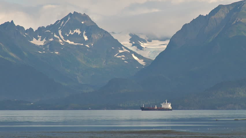 Zoom out from oil tanker anchored in bay to glaciers and mountains, the bay, and