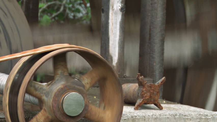 Close-up of drive pulley for grindstone, water-driven wheel in background.