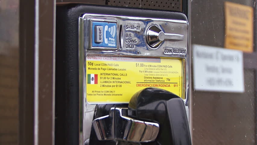 Inserting quarters into the slot of a pay phone. Close-up.
