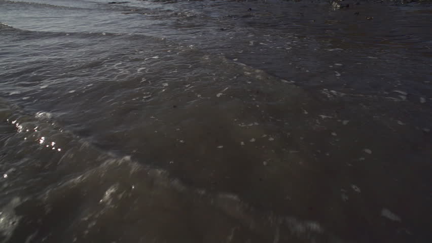 Camera hovering just over muddy waves of Kachemak Bay at Mud Bay Beach as tide