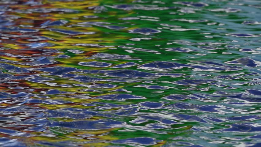 Multicolored reflections in the ripples of harbor water in slow motion.