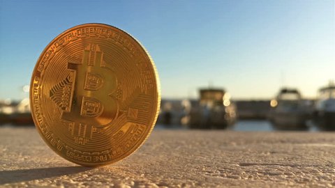 Golden bitcoin on stone wall in harbor with boats at background close up outdoor
