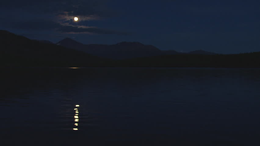 Moon beam reflected on dark lake waters, hill in the background. Moon reflection